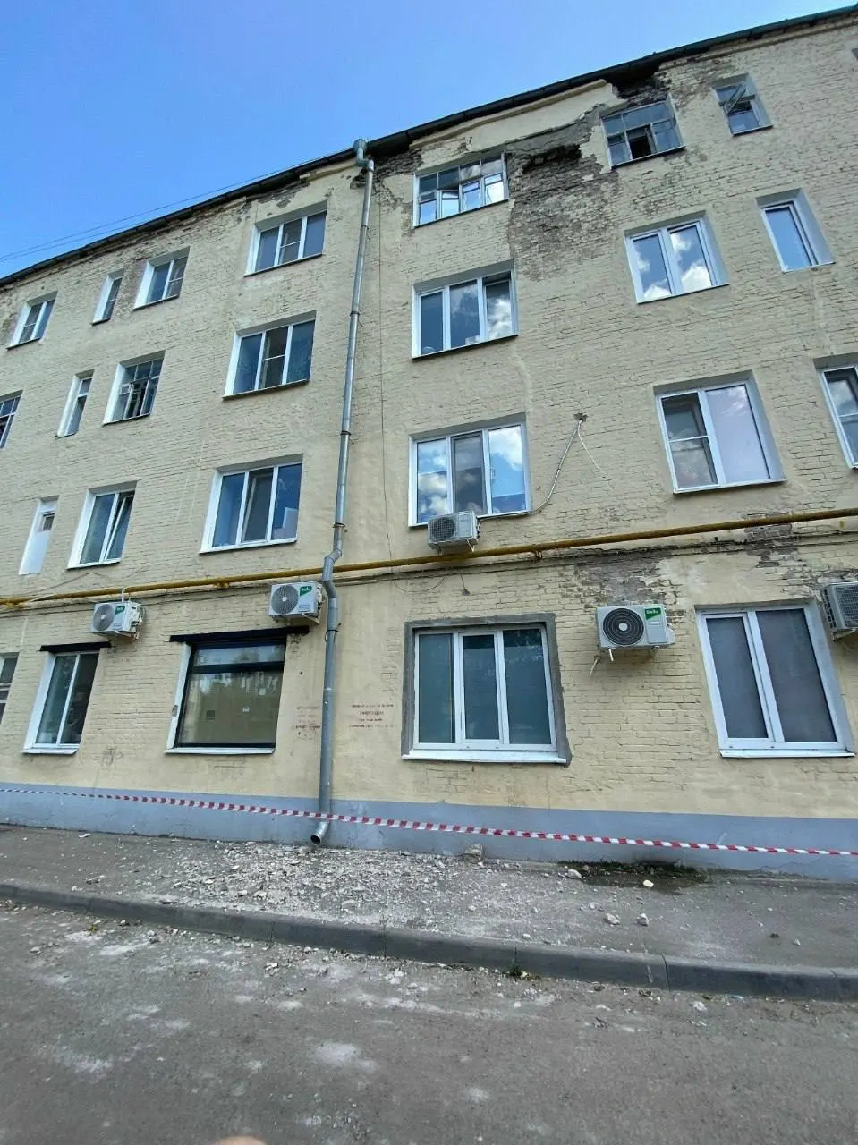 Из фасада дома сыплются куски бетона. УК натянула ленту, но прохожим в дождь приходится идти под падающими обломками — остальные проходы затоплены.